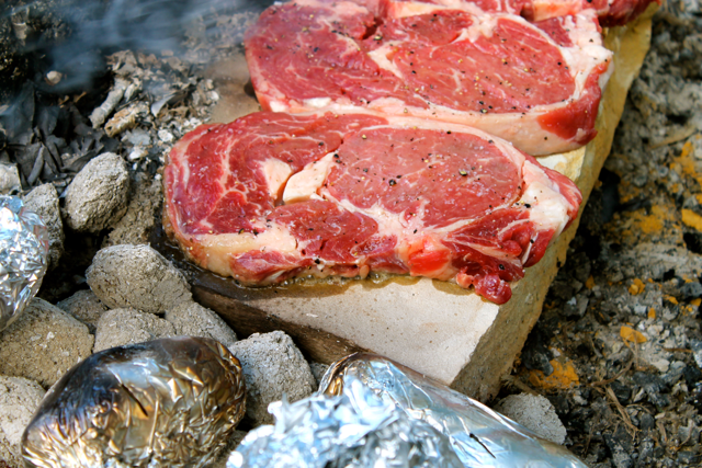 steaks cooking on campfire rocks